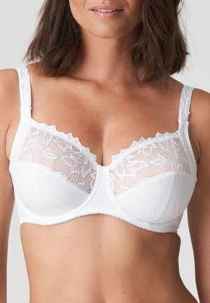 White bra featuring a sheer lace overlay with floral patterns, padded cups, and textured stitching. Adjustable straps and scalloped edges visible.