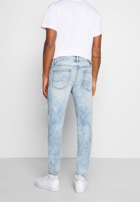 Vaqueros de mezclilla azul claro con acabado desteñido, pierna estrecha y detalles desgastados. Los bolsillos traseros presentan un diseño clásico de costura.