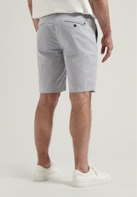 Shorts légers à rayures bleues et blanches avec deux poches arrière, fermetures à boutons et coupe droite, associés à des sneakers blanches.