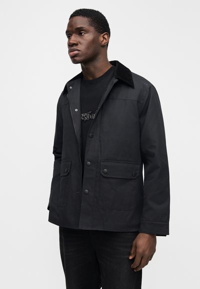 Μαύρο σακάκι με γιακά από κοτλέ ύφασμα, κουμπώματα με κουμπιά και δύο μπροστινές τσέπες. Το υλικό φαίνεται ανθεκτικό με απαλή υφή.