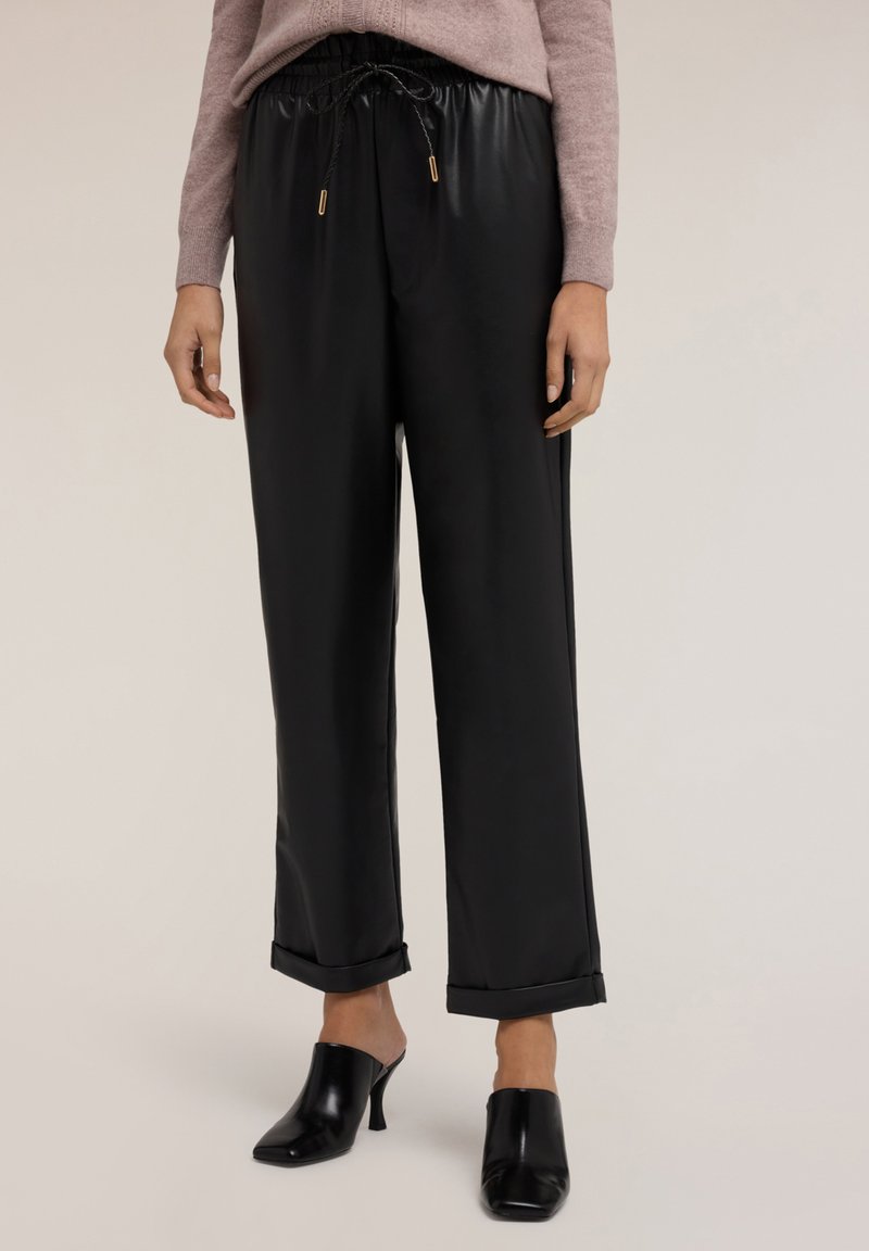 Černé kalhoty z imitace kůže s volným střihem, stahovacími šňůrkami v pase a ohrnutými manžetami. Nosí se s černými muly na podpatku.