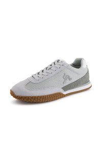 Zapatilla deportiva de color gris claro con paneles de malla y ante, suela de goma con un agarre texturizado y una franja blanca como acento.