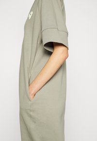 Jasnoszara sukienka krótko rękawowa o luźnym kroju, z bocznymi kieszeniami i małym logo na piersi, wykonana z miękkiego materiału bawełnianego.