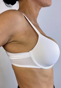 Sujetador deportivo blanco con tela suave y lisa, copas moldeadas y amplios laterales de malla para transpirabilidad. Tirantes finos ajustables y diseño sin costuras.