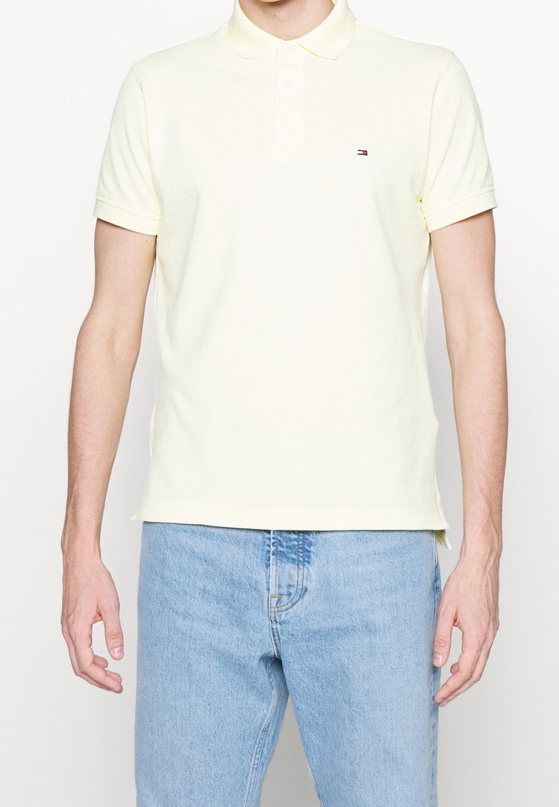 Polo jaune clair en coton, avec un tissu subtilement texturé, manches courtes et un petit logo sur la poitrine. Associé à un jean en denim.