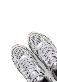 Baskets de sport argentées avec une tige en mesh, des accents verts et des semelles en caoutchouc. Lacets à texture lisse avec des détails en matériel réfléchissant.