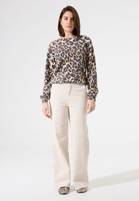 Pull en imprimé léopard en matière douce, manches longues, col rond. Associé à un pantalon ample crème et des chaussures métalliques.