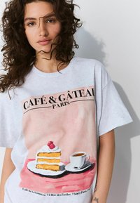 Siva pamučna majica s kolorističkom ilustracijom komada torte i šalice kafe na ružičastoj pozadini s crnim natpisom.