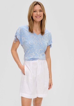 Lichtblauw kort mouwtop met bloemenpatroon, v-hals en geplooide mouwen; gecombineerd met witte linnen shorts met zijzakken.