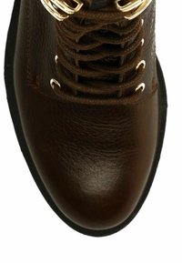 Botte en cuir marron avec une finition texturée, dotée de lacets marron, d'œillets en ton or et d'un design à bout rond. Semelle en caoutchouc noir.