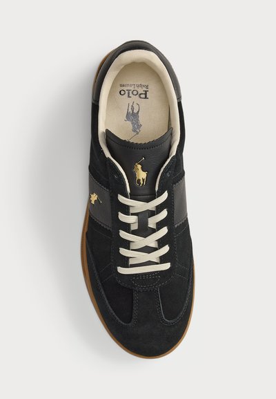 Adidași negri din suede, cu șireturi crem, accente de piele și un logo auriu. Talpa este de culoare gumă, cu un design texturat.