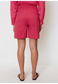 Shorts de algodón rosas con una cintura de media altura, bolsillos laterales y un bolsillo trasero. Llevados con una camiseta rosa a juego y sandalias.