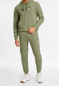 Sweat à capuche vert olive avec logo noir sur la poitrine, assorti d'un pantalon de survêtement de la même couleur. Les deux sont fabriqués en tissu doux avec des poignets côtelés et des poches.