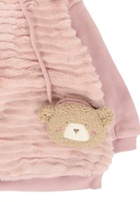 Veste en polaire rose avec un tissu texturé à volants, dotée d'une poche en forme d'ours en beige doux avec des détails faciaux brodés.