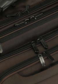 Gros plan sur plusieurs rails de fermeture éclair noirs avec curseurs noirs sur un tissu texturé foncé, montrant les coutures détaillées et les mécanismes de la fermeture éclair.