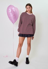 Dryžuota ilgomis rankovėmis marškinėliai bordo ir baltos spalvos, derinami su tamsiai raukšlėta sijona. Juodi platforminiai batai ir rožinis širdelės formos balionas.