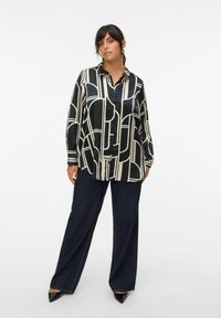 Black and cream patterned button-up shirt with a loose fit, paired with dark wide-leg jeans and pointed black heels.