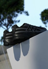 Čierne športové topánky s sieťovanými panelmi, tromi akcentujícími pruhmi, textúrovanou podrážkou a polstrovaným opätkom, položené na bielom povrchu.