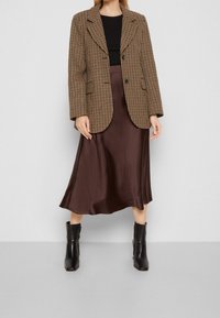 Ruskea houndstooth-takkia mustan paidan päällä, yhdistetty tummaan ruskeaan satiini-midi-hameeseen ja mustiin nilkkureihin. Huomattava rakenne ja tekstuuri.