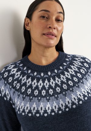 Marineblå strikket sweater med rund hals, der har et lysblå og hvidt geometrisk mønster henover brystet og skuldrene.