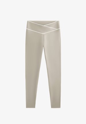 Svetlo bež legice z mehkim in gladkim materiali, ki imajo obliko pasu v križcu in kontrastne bele obrobe.