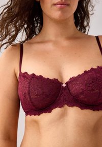 Burgundy lace bra with underwire, featuring scalloped edges, adjustable straps, and a small rose detail at the center.