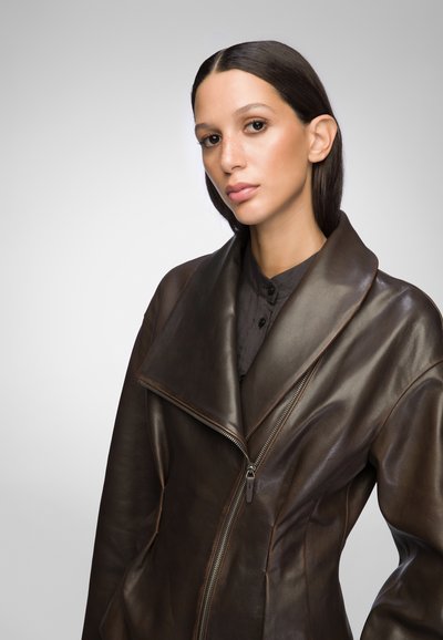 Brown leather jacket with a large collar, zip closure, and fitted design. The material has a smooth texture with subtle sheen and stitching details.