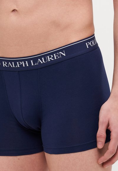 Tummansininen puuvillainen bokserialushousu, jossa on istuva malli. Housuissa on erottuva vyötärönauha, jossa lukee valkoisella tekstillä "Polo Ralph Lauren".