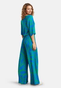 Blauwe jumpsuit met een groen abstract patroon, met losse mouwen, een ingezette taille en wijde broekspijpen. Gemaakt van lichtgewicht stof.
