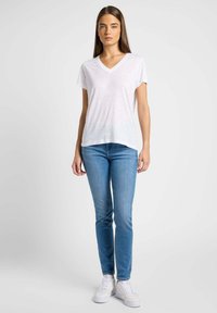 Camiseta blanca de manga corta y cuello en V, de tejido ligero, combinada con jeans ajustados de color azul claro y zapatillas blancas. Un look simple y casual.