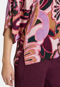 Farverig, mønstret bluse med pink, grønne og lilla nuancer, løse ærmer og sideslids; lavet af letvægtsstof.