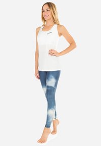Weißes Tanktop mit schwarzem Logo, kombiniert mit blauen Leggings im Wolkenmuster. Beide Kleidungsstücke sind figurbetont und aus dehnbarem Material gefertigt.