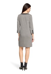 Zwart-wit geruite jurk met driekwartmouwen en een boothals. De achterkant heeft een centrale naad en zijsplitten bij de zoom.