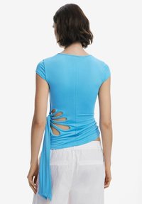 Haut ajusté bleu clair avec des manches courtes, détail torsadé et découpes sur les côtés, doté d'un accent noué à la taille. Tissu doux et extensible.