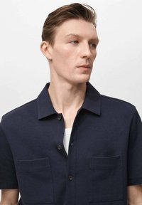 Donkerblauwe shirt met korte mouwen en een button-down kraag, voorzien van twee voorzakken en een gladde structuur.