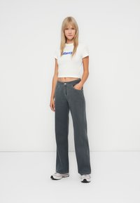 Gray wide-leg jeans with a high waist, featuring front pockets and contrasting stitching. Paired with a white cropped t-shirt and sneakers.