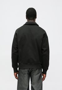 Sweatshirt preta com gola larga, corte descontraído e punhos canelados. Acompanhada por calças de ganga escuras com design de perna reta.