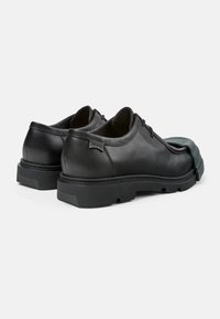 Schwarze Lederschuhe mit runder Spitze, dicken Gummisohlen und einem einzigartigen grünen Akzent an der Spitze. Minimalistisches Design mit genähten Details.