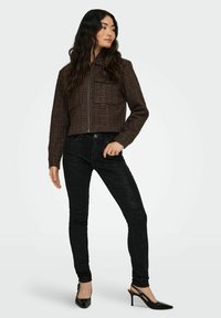 Pruun lühike jakk tekstuurse kangaga ja kahe eesmise taskuga, kombineeritud mustade kitsaste teksapükste ja mustade rihmikudega.