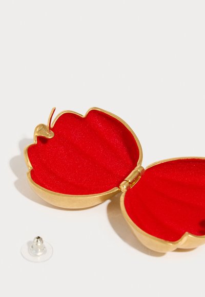 Μικρό κουτί σε χρυσό χρώμα με σχήμα πεταλούδας, με κόκκινη βελούδινη εσωτερική επένδυση. Περιλαμβάνει διάφανο αναρροφητήρα για προσκόλληση.