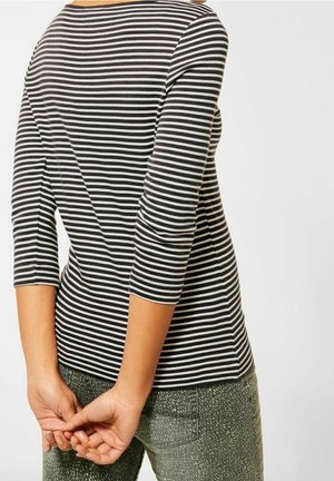 Haut à rayures noir et blanc à manches longues, présentant un décolleté large et une silhouette ajustée, accompagné de pantalons verts texturés.