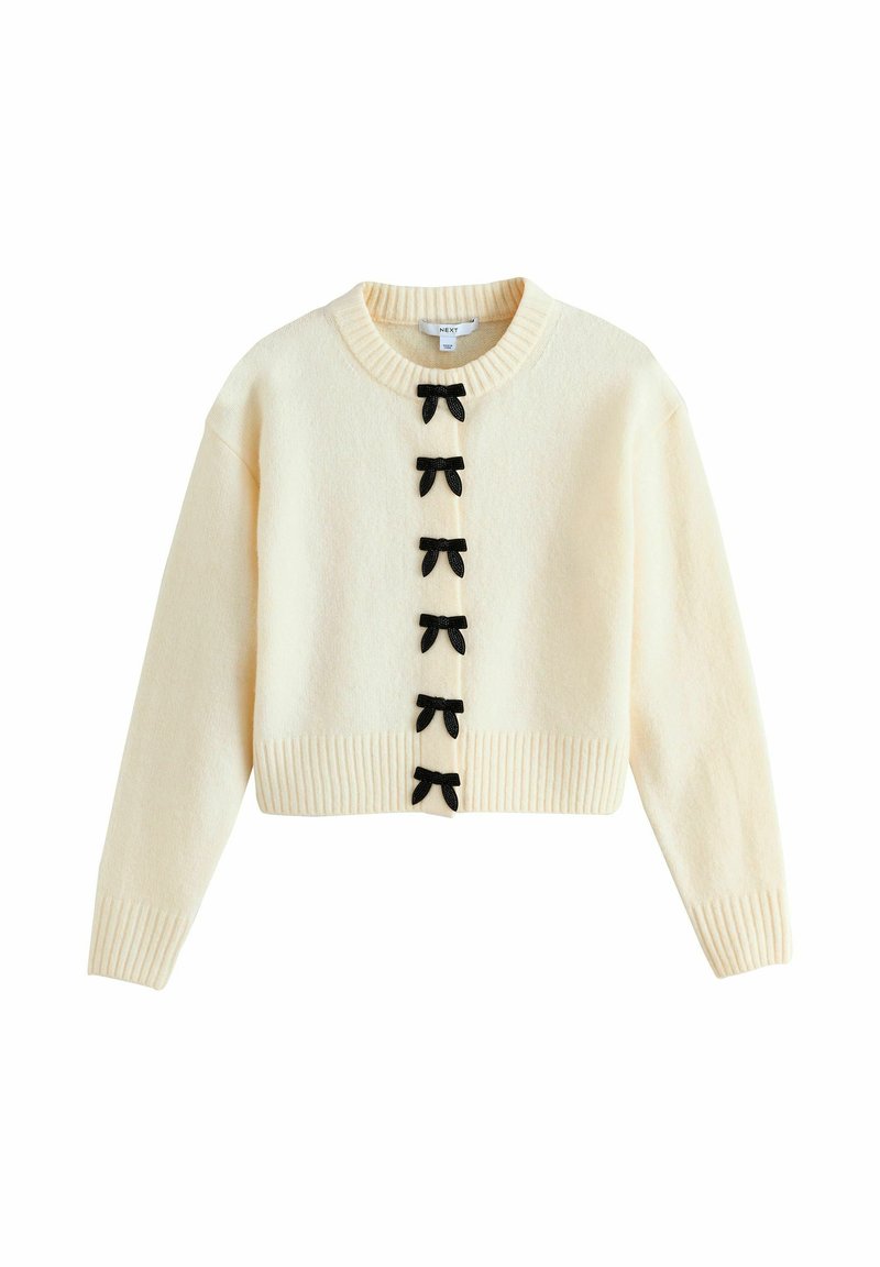 Maglione corto crema con scollo rotondo, caratterizzato da decorazioni a fiocco nere lungo la parte anteriore, polsini a coste e un tessuto a maglia testurizzato.