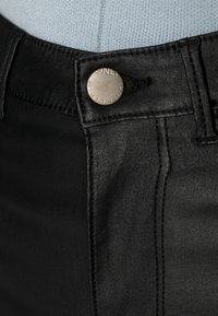 Jean en denim noir avec un design classique à cinq poches, une fermeture par bouton en métal et des coutures contrastées le long des coutures.