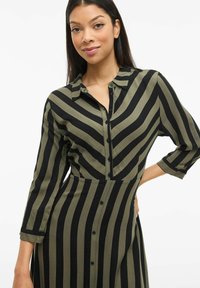 Šaty na gombíky s vertikálnymi čierno-olivovými pruhmi, dlhými rukávmi a priliehavým strihom so zaobleným golierom.