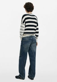 Maglione a righe in navy e bianco, abbinato a jeans in denim blu a vestibilità ampia con tasche posteriori e dettagli di cucitura sottili.