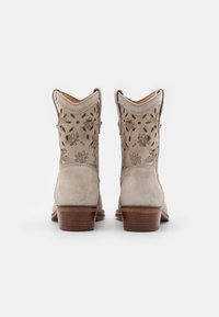 Beige suede cowboy boots with floral embroidery on the shaft and a brown wooden heel, featuring a pointed toe and curved top edge.