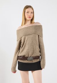 Beige off-shoulder genser med ribbestrikket halslinning, lange ermer og et svart miniskjørt. Akkentuert med et flettet brunt belte og sølvspenne.