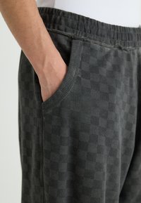 Gray checkerboard-patterned sweatpants with an elastic waistband and side pockets, featuring a soft texture and relaxed fit.