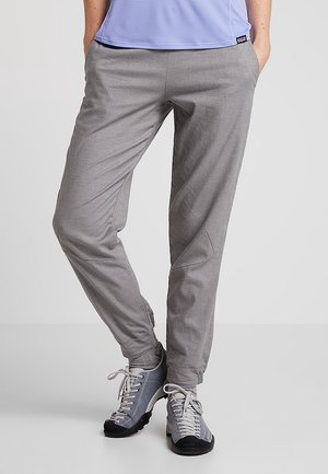 Dolna część ciała osoby ubranej w jasnoszare, casualowe spodnie, szare skarpetki i szare tenisówki na sznurowadła, stojącej z rękami w kieszeniach.