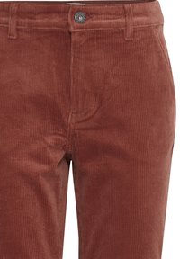 Pantalons en velours côtelé de couleur rouille avec des côtes verticales, dotés d'une fermeture à bouton en métal et d'un design classique à cinq poches. Texture douce.